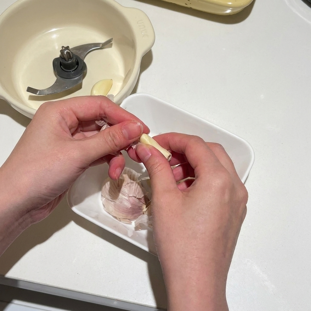 Hände schälen frische Knoblauchzehen und geben sie in einen elektrischen Zerkleinerer.