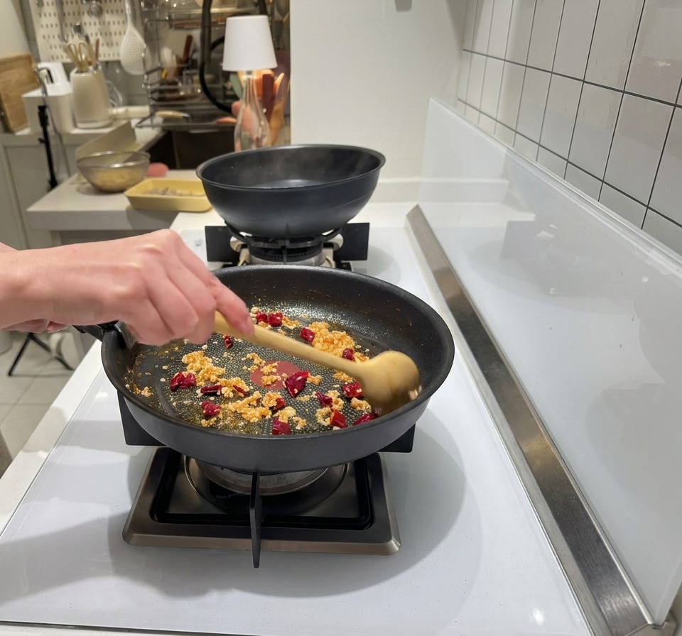 Gehackter Knoblauch und Chili werden in das rötlich gefärbte Garnelenöl in der Pfanne gerührt.