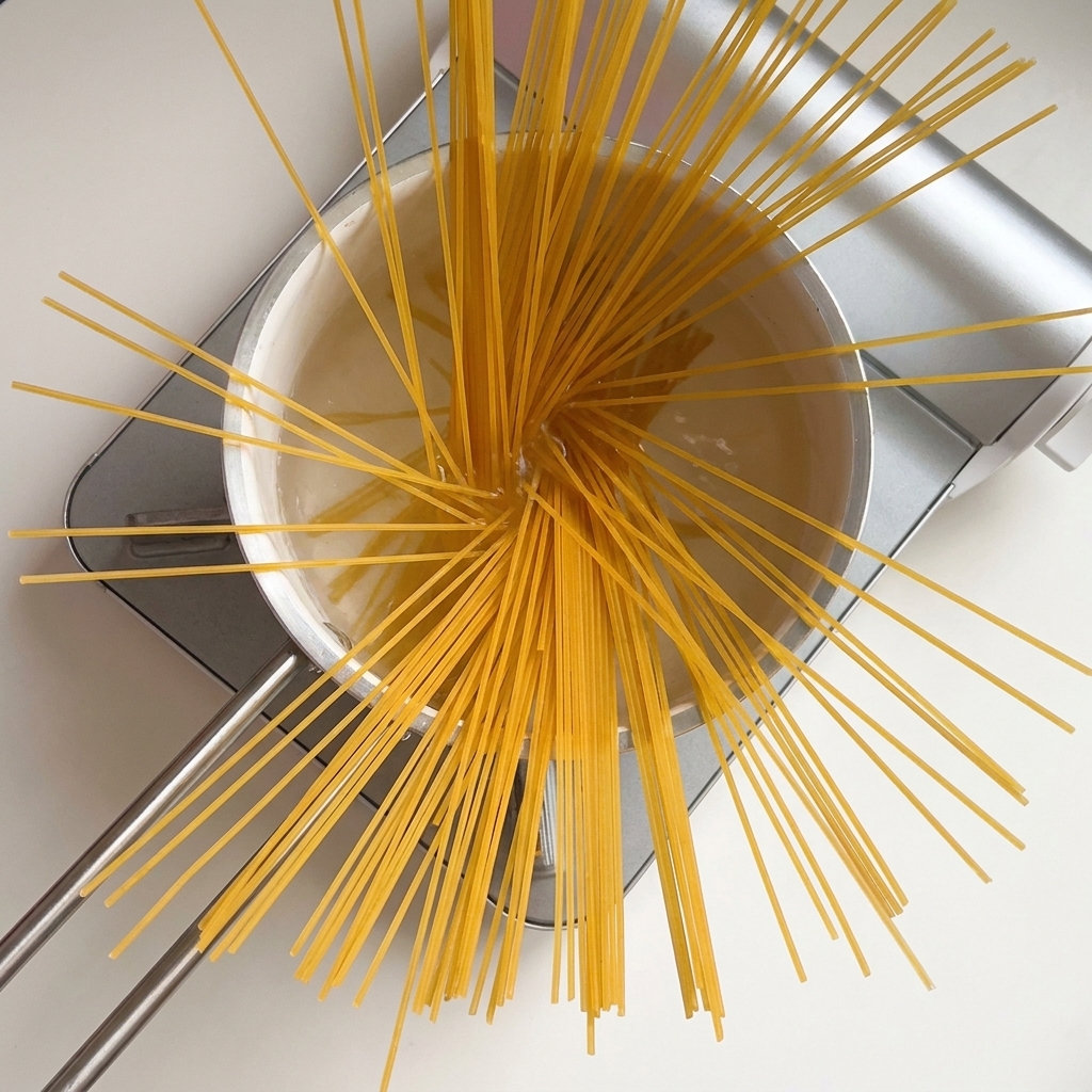 Getrocknete Spaghetti fächerförmig in einem Topf mit kochendem Wasser.