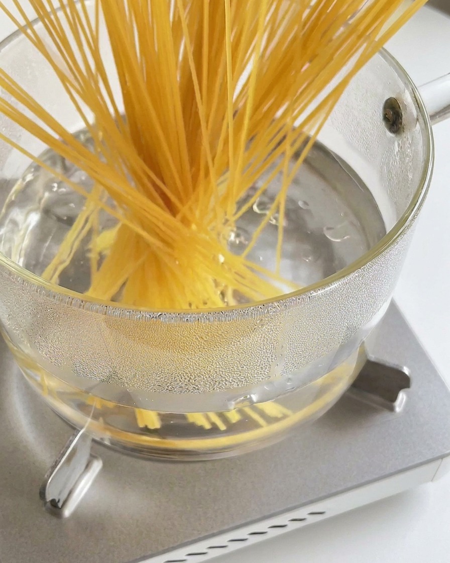 Ein Bündel langer, trockener Spaghetti wird in einen Topf mit kochendem Wasser gegeben.
