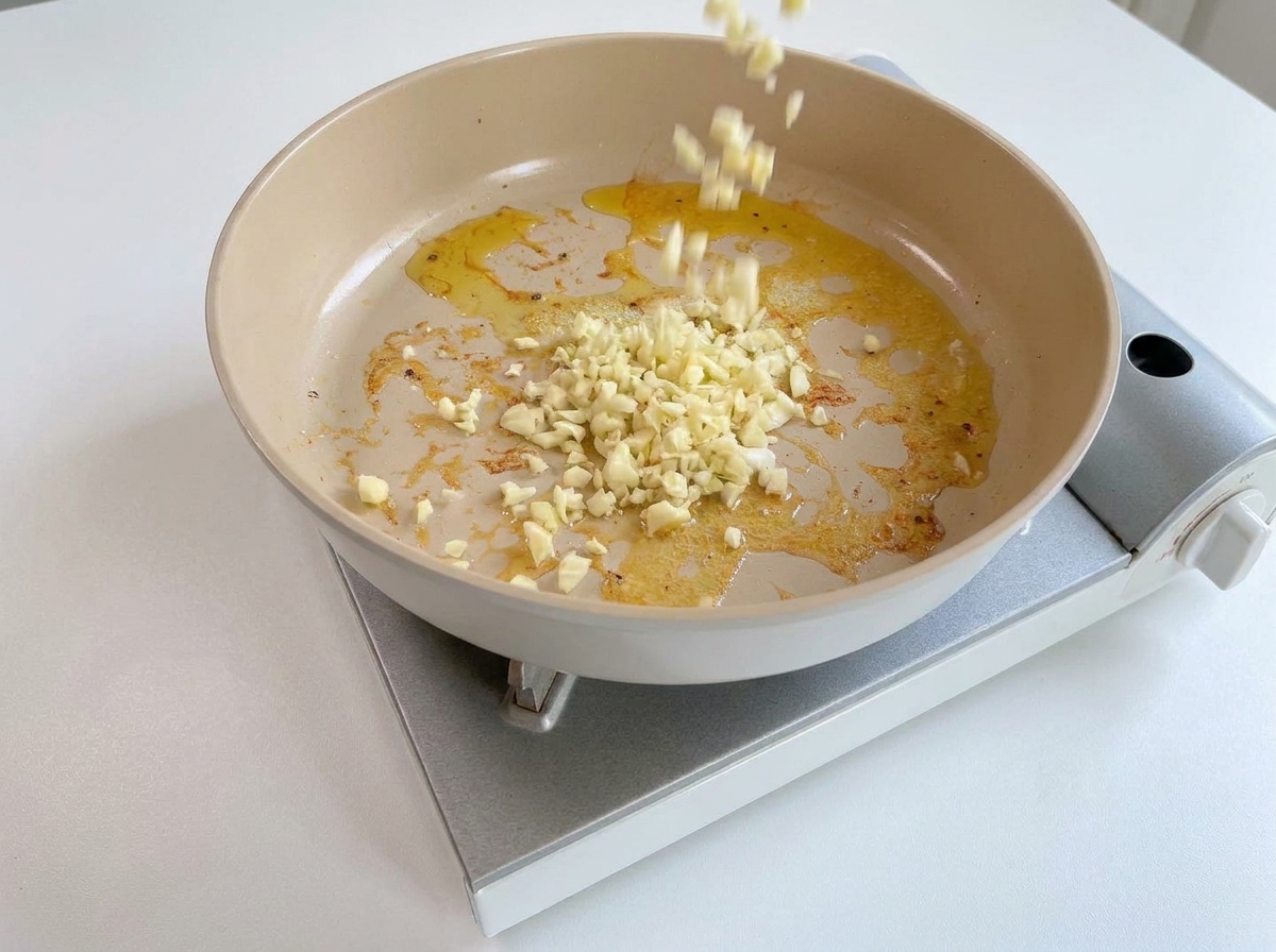 Gehackter Knoblauch wird in die Pfanne mit den Resten von Öl und Butter gegeben.