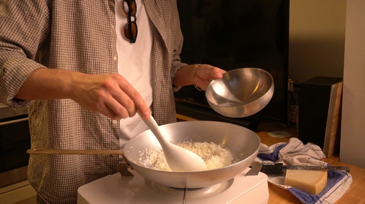 Warmes Wasser wird aus einer kleinen silbernen Schale in eine Pfanne mit frisch geriebenem Pecorino-Käse gegossen.