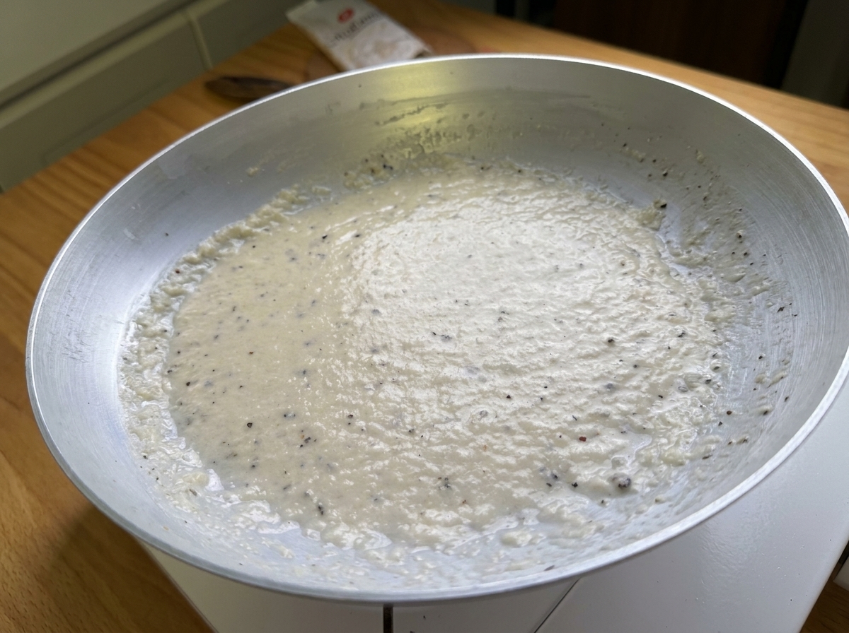 Nahaufnahme einer glatten, cremigen Paste aus Pecorino-Käse und schwarzem Pfeffer in einer Pfanne.