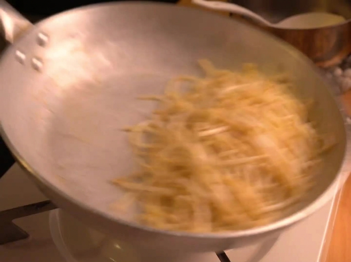 Spaghetti werden kräftig in einer silbernen Pfanne geschwenkt, wodurch die cremige Sauce emulgiert.