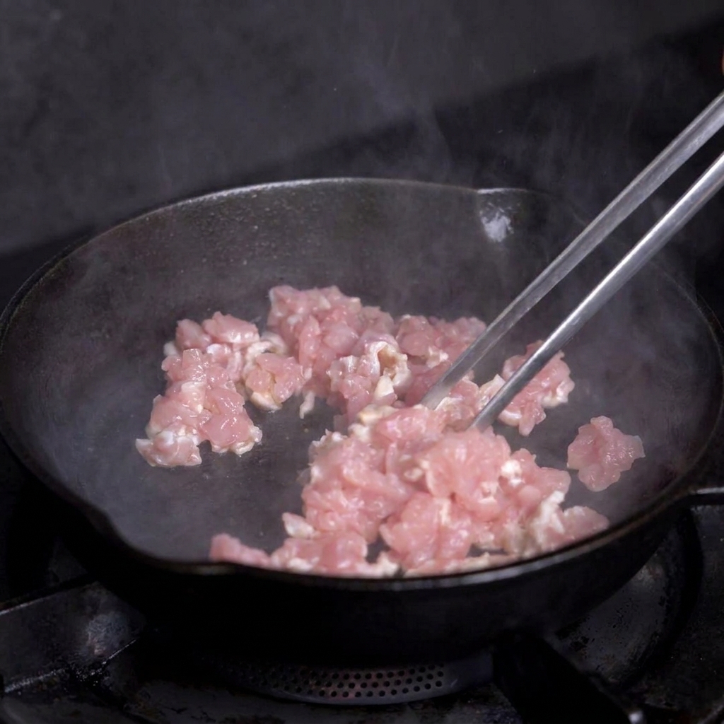 Gewürfeltes Fleisch wird in einer heißen Pfanne mit einer Zange angebraten.