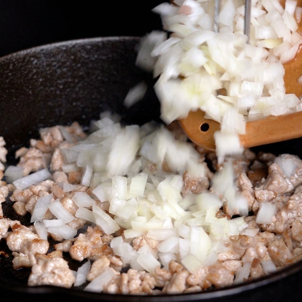 Gehackte weiße Zwiebeln werden vom Schneidebrett zum Fleisch in die Pfanne gegeben.