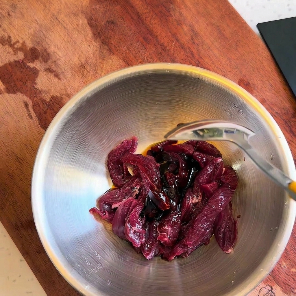 Dunkle Würzsauce wird mit einem Löffel über die Rindfleischstreifen in der Schüssel gegossen.