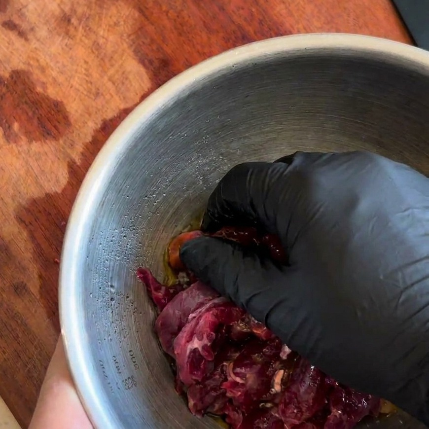 Eine Hand vermengt die Fleischstreifen gründlich mit der dunklen Marinade.