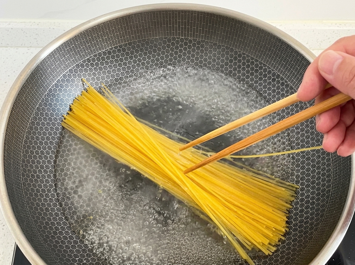Trockene Spaghetti werden mit Stäbchen in einen Wok mit kochendem Wasser gedrückt.