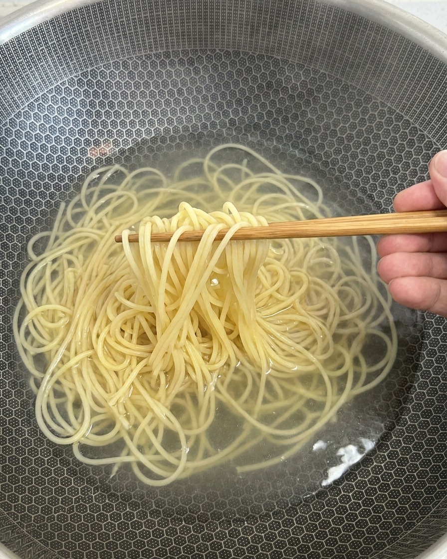 Gekochte Spaghetti werden mit einer Zange aus dem heißen Wasser gehoben.