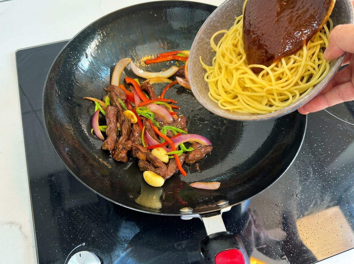 Gekochte Spaghetti und Fleischmischung werden im Wok kombiniert.