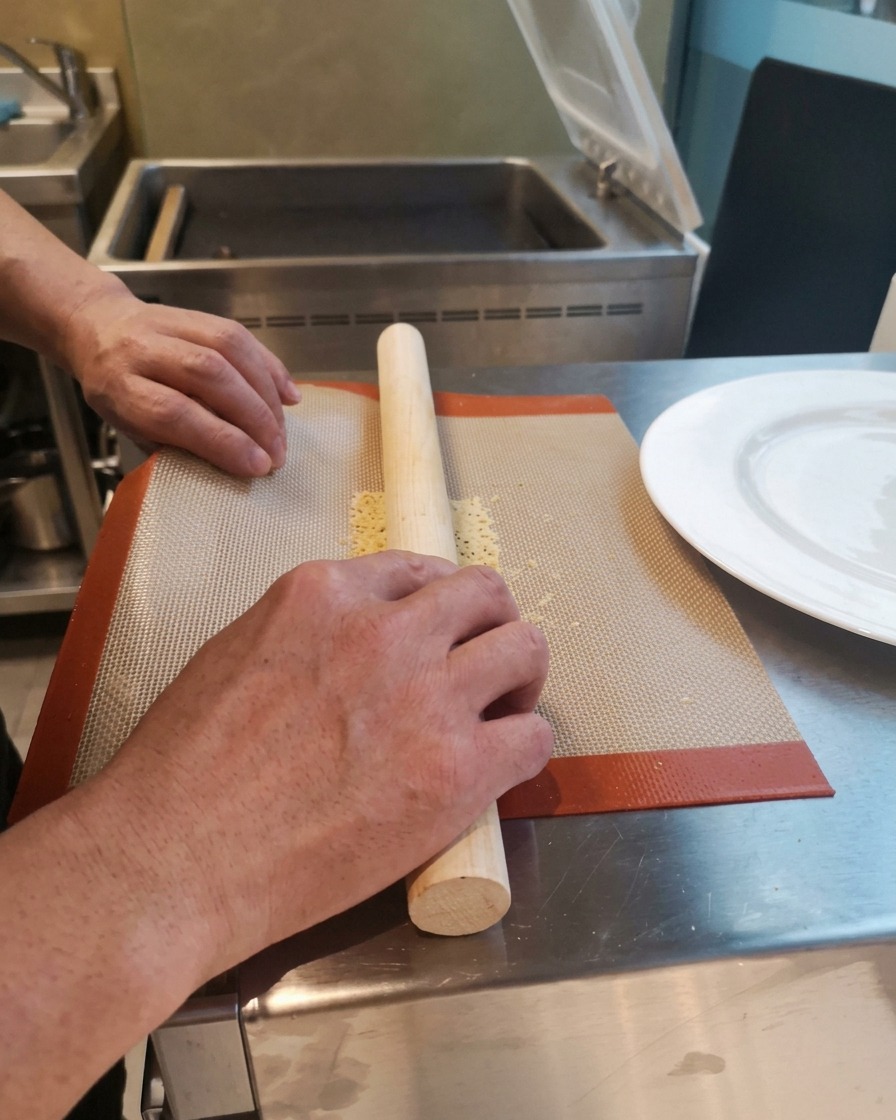 Hände rollen einen heißen, biegsamen Käsechip vorsichtig um ein Nudelholz aus Holz direkt auf der Silikonmatte.