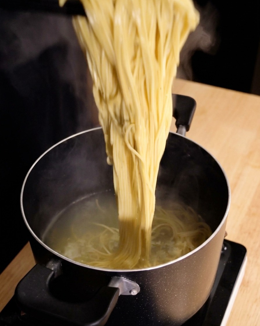 Dampfende Spaghetti werden mit einer Küchenzange direkt aus dem Kochtopf gehoben.