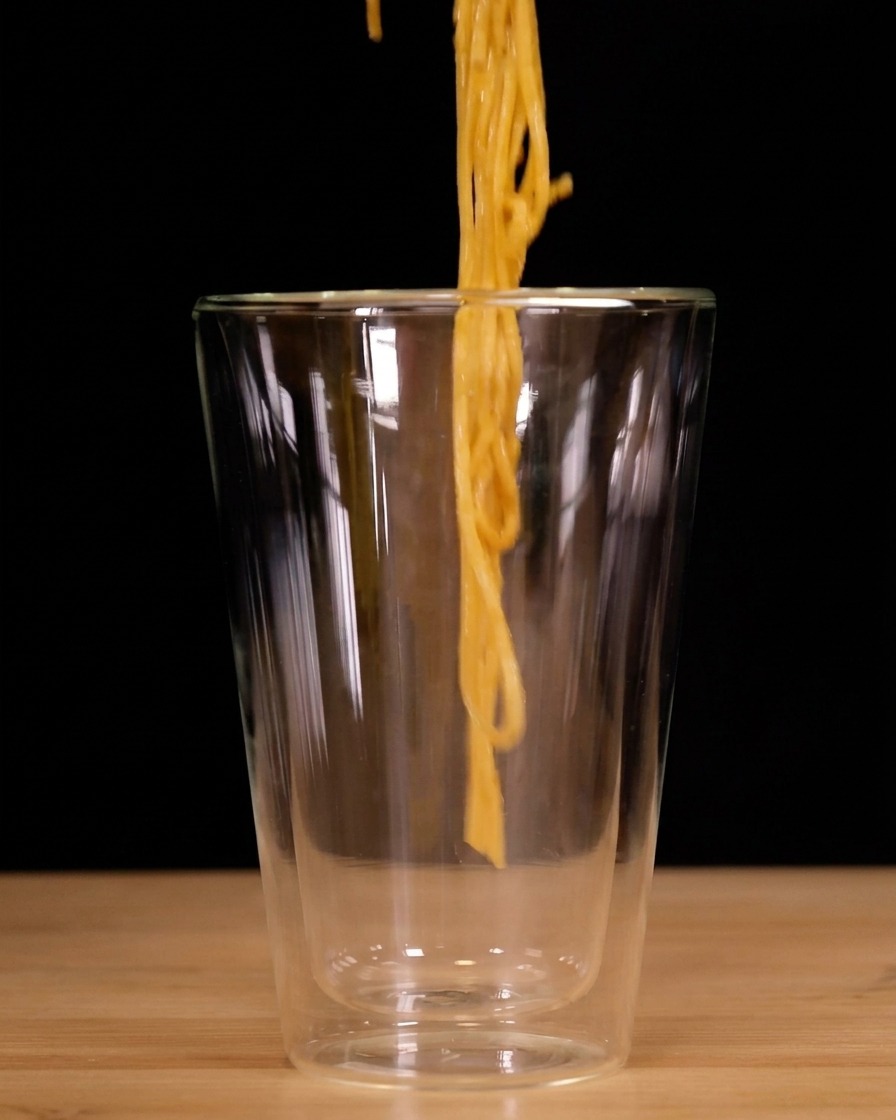 Spaghetti werden mit einer Zange aufgedreht und in ein hohes Doppelwandglas gesetzt.