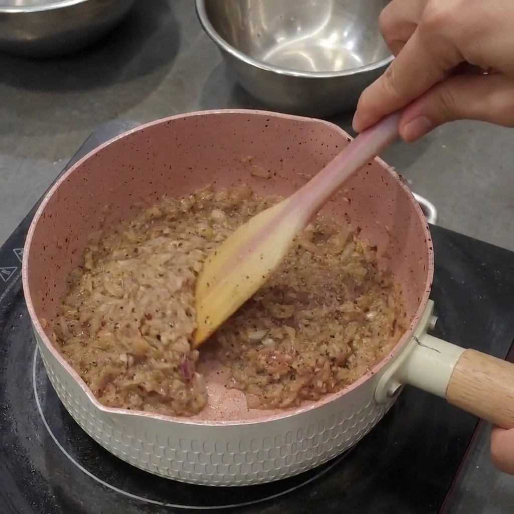 Schwarzer Pfeffer wird in die Zwiebelmischung gerührt, wodurch eine dunkle, grobe Paste entsteht.