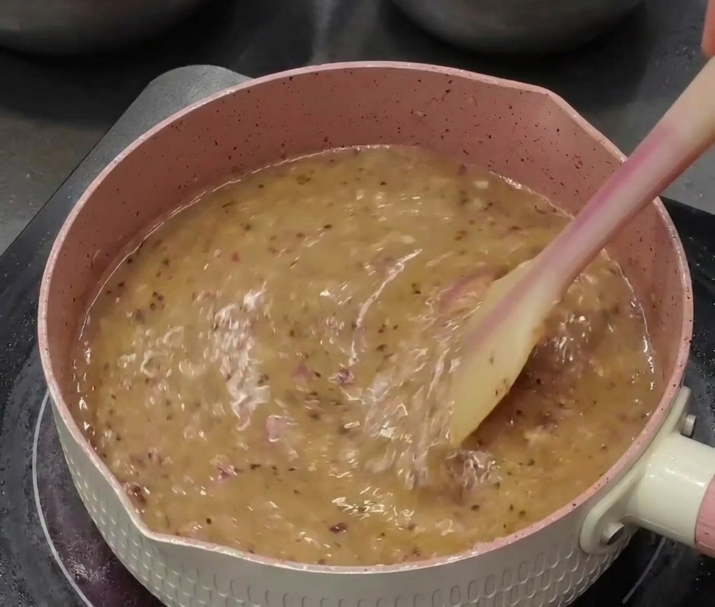 Die wässrige Pfeffersauce sprudelt in einem Topf und wird mit einem Silikonspatel umgerührt.