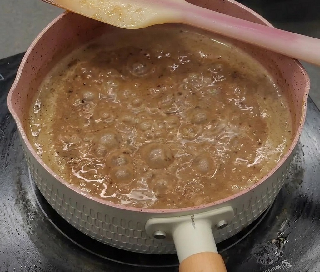 Eine dicke, glänzende, dunkelbraune Pfeffersauce köchelt kräftig in einem Topf.