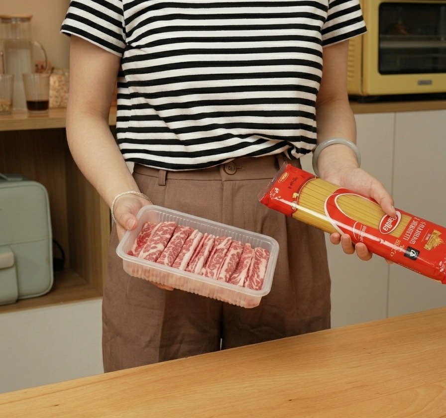 Eine Person hält eine Packung Spaghetti und eine Schale mit dünnem Rindfleisch.