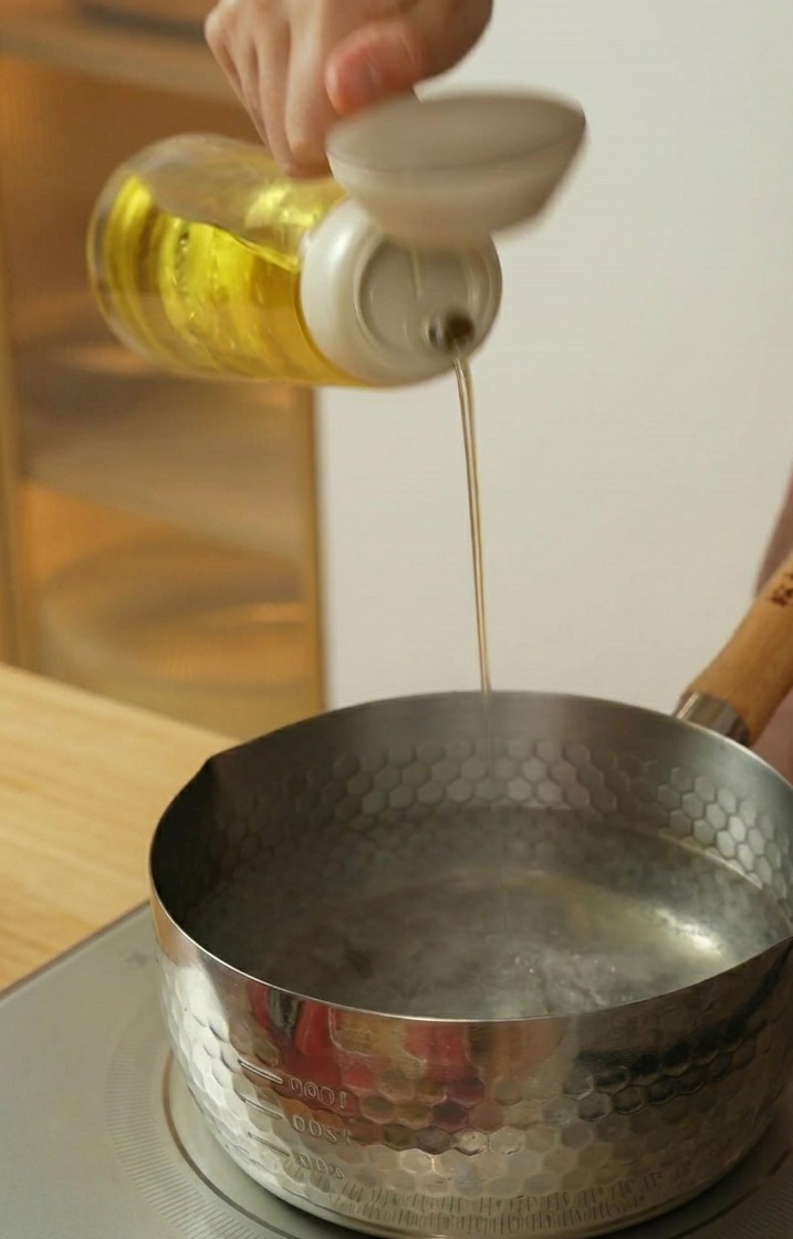 Speiseöl wird aus einer Flasche in einen Topf mit kochendem Wasser gegossen.