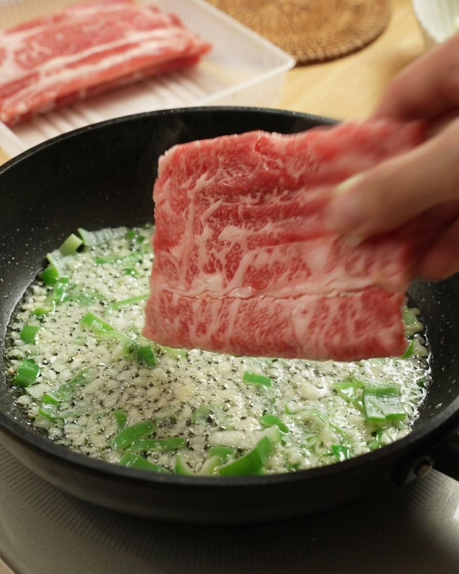 Rohes Rindfleisch wird zu den Frühlingszwiebeln und dem Knoblauch in die Pfanne gegeben.