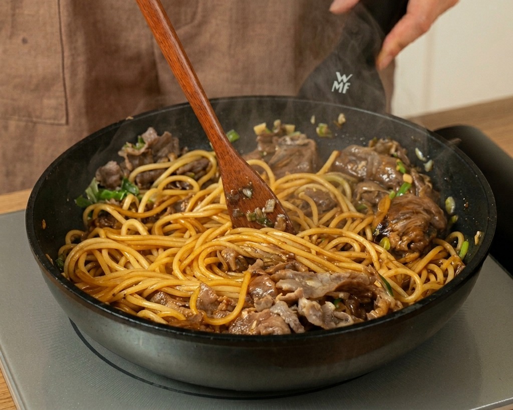 Spaghetti, Fleisch und Sauce werden mit einem Holzspatel in der Pfanne vermischt.
