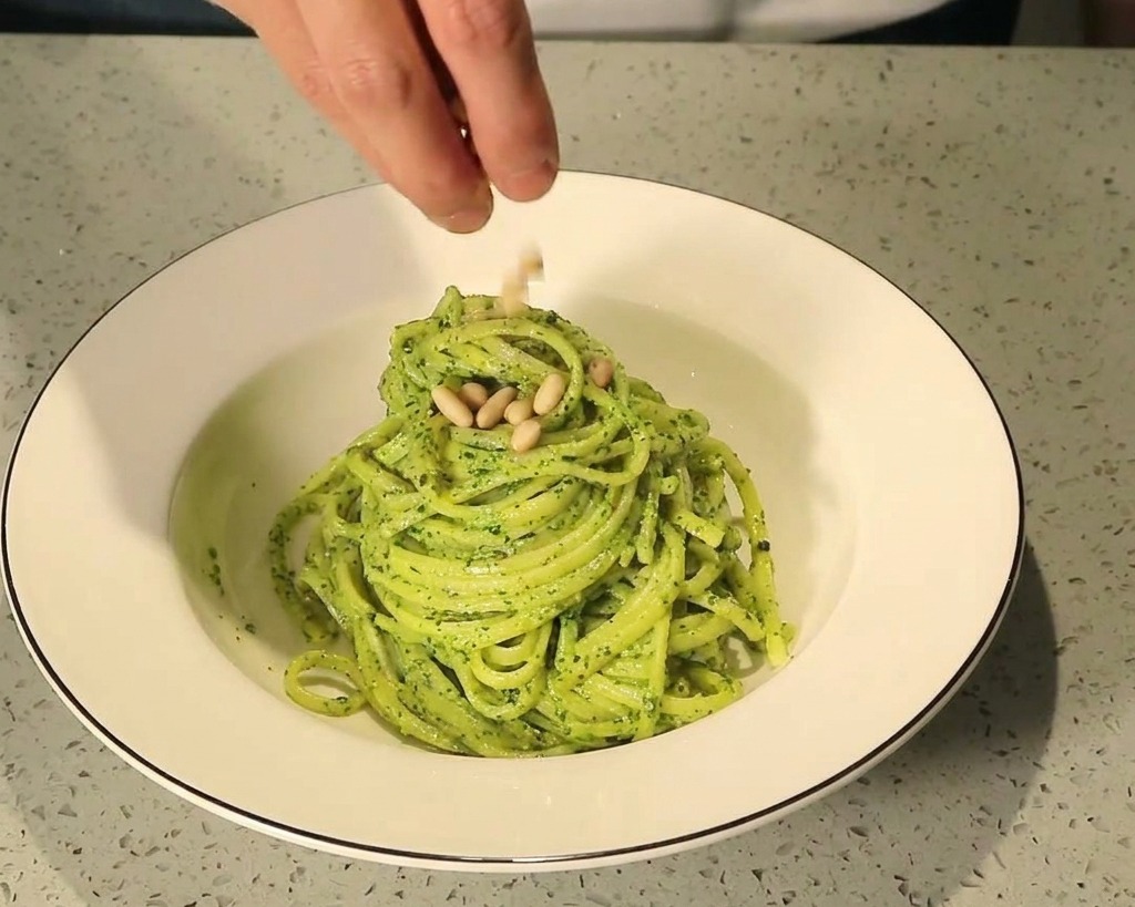 Pinienkerne werden über ein Nest aus Pesto-Pasta in einer weißen Keramikschüssel gestreut.
