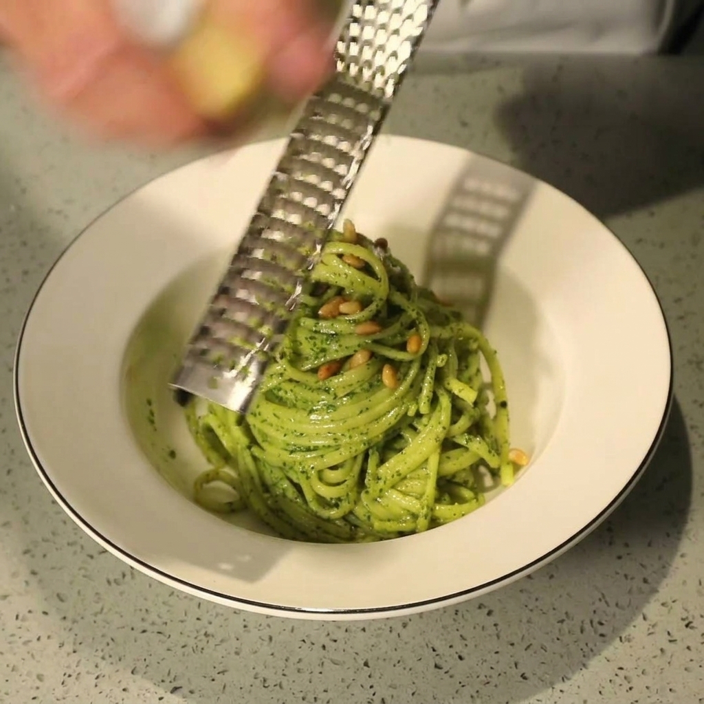 Frischer Parmesan wird mit einer Reibe über die fertig angerichtete Pasta-Schale gehobelt.