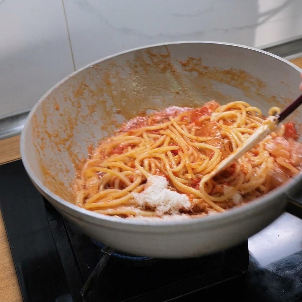 Bucatini werden in einer weißen Pfanne kräftig mit der Sauce und dem Käse vermengt.