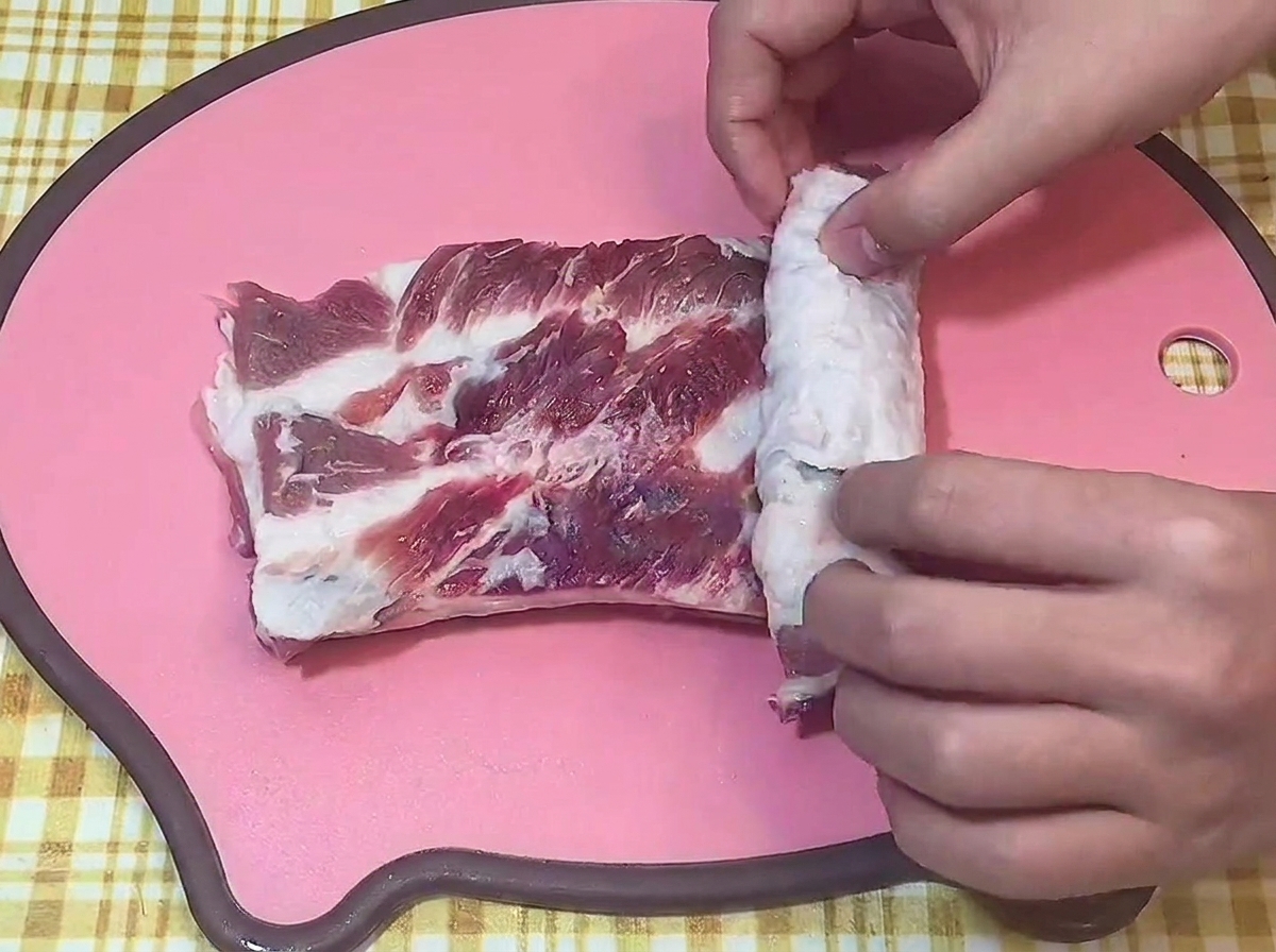 Hände rollen ein Stück Schweinebauch fest zu einer Rolle auf einem Brett.