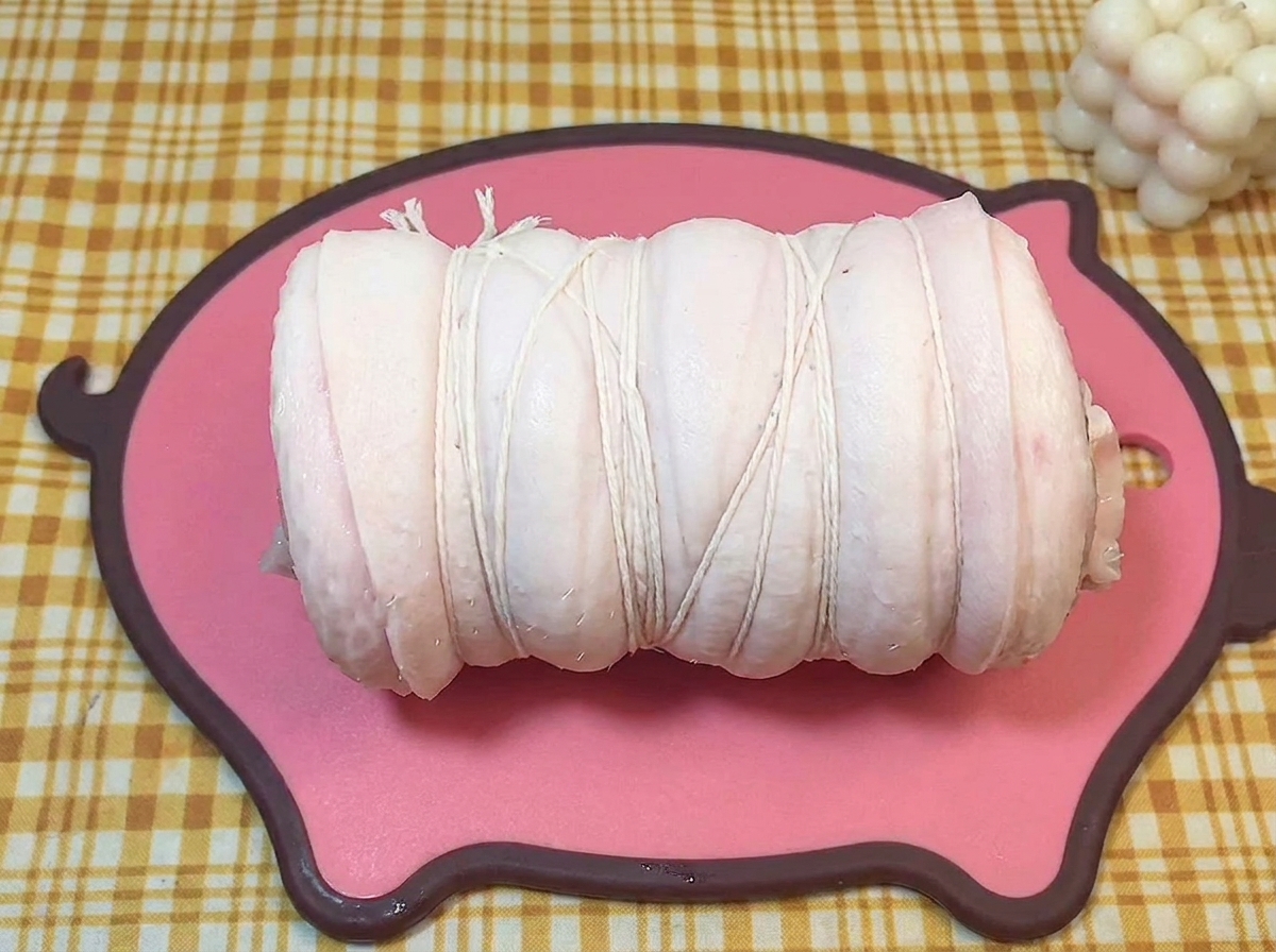 Ein mit weißem Küchengarn fest verschnürter Schweinebauch auf einem Brett.