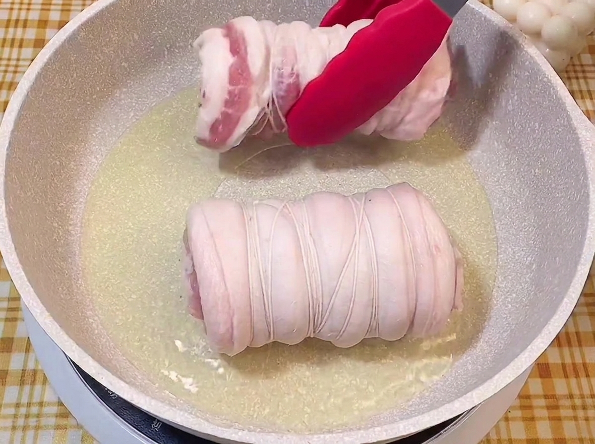 Eine Grillzange legt die Fleischrollen in eine heiße Pfanne mit Öl.