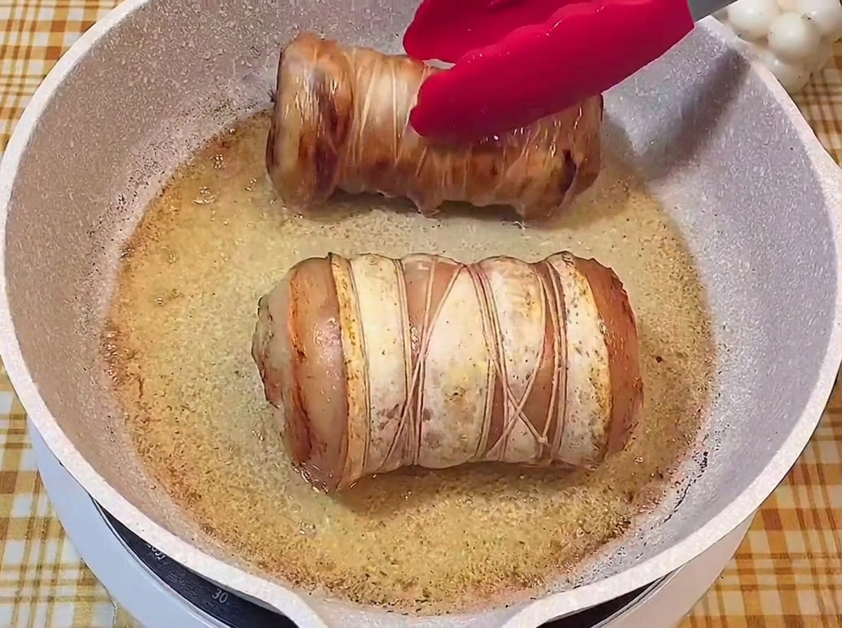 Zwei goldbraun angebratene Fleischrollen brutzeln in der Pfanne.