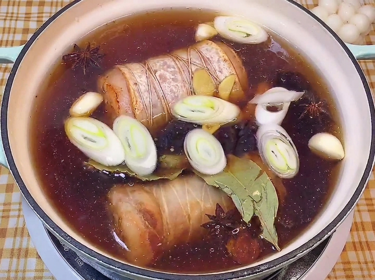 In dunkler Sojasauce köchelnder Schweinebauch mit Lauch und Gewürzen.