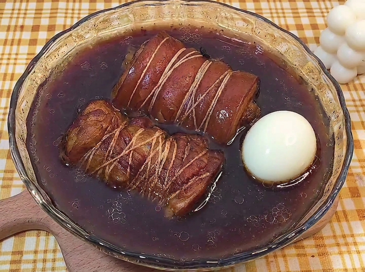 Zwei Rollen Chashu und ein gekochtes Ei marinieren in einer dunklen Flüssigkeit.