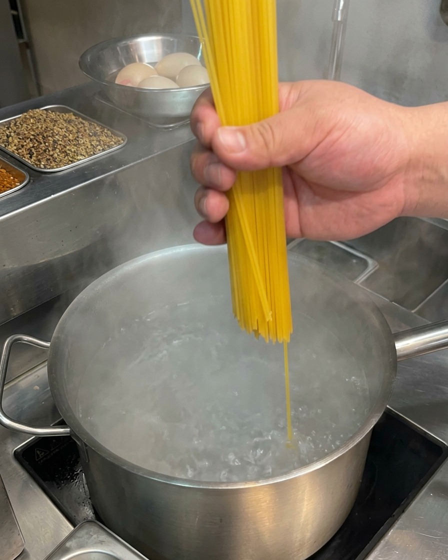 Spaghetti werden in einen Topf mit sprudelnd kochendem Wasser gegeben.