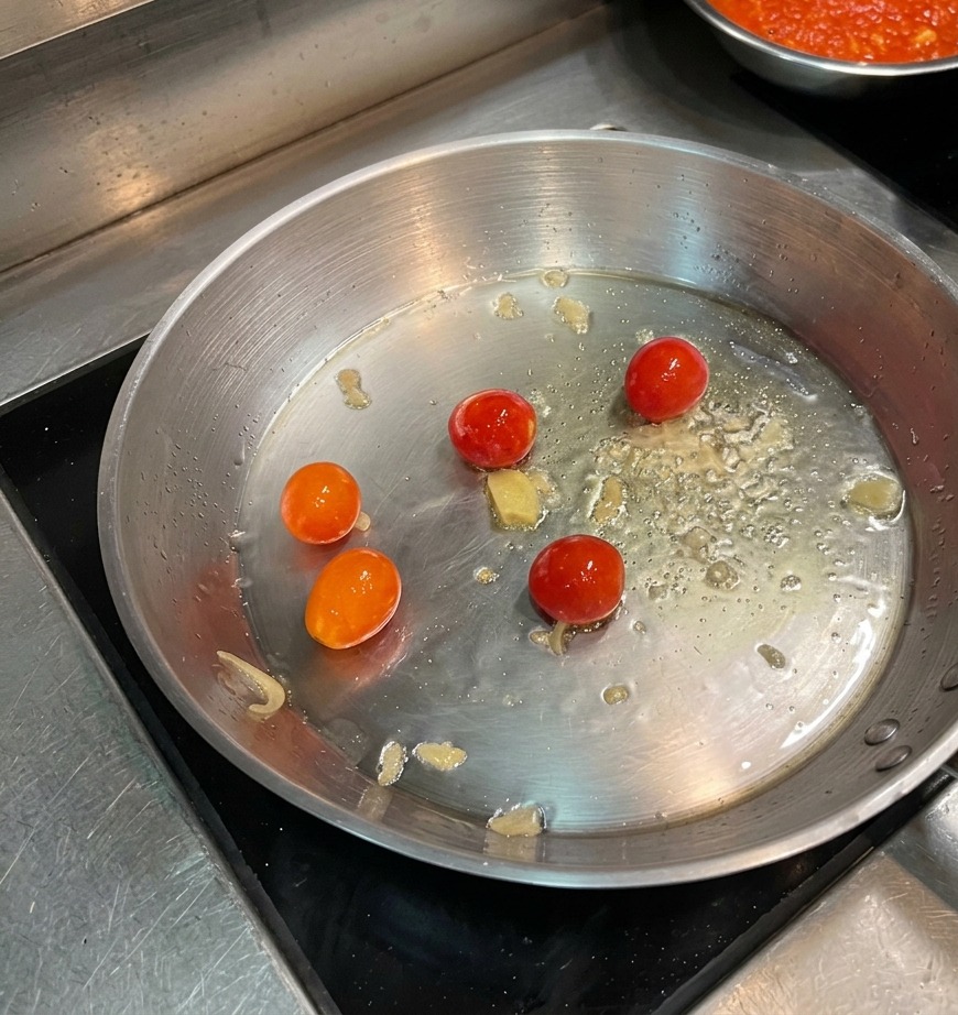 Kirschtomaten brutzeln in heißem Öl in einer Edelstahlpfanne.