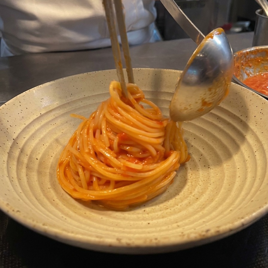 Spaghetti werden mit einer Zange und einer Schöpfkelle zu einem Nest gedreht.