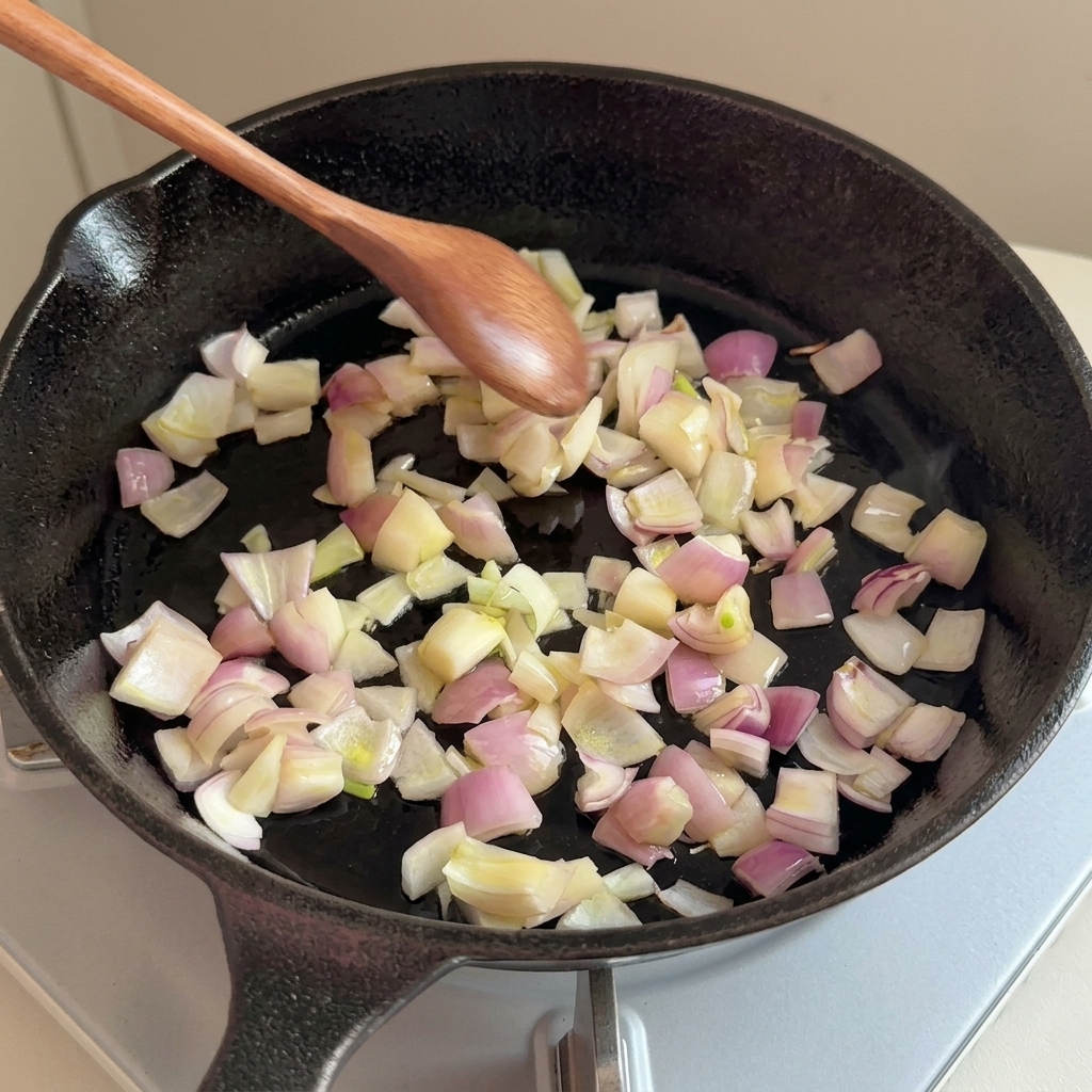 Gehackte Zwiebeln werden mit einem Holzlöffel in einer gusseisernen Pfanne angebraten.