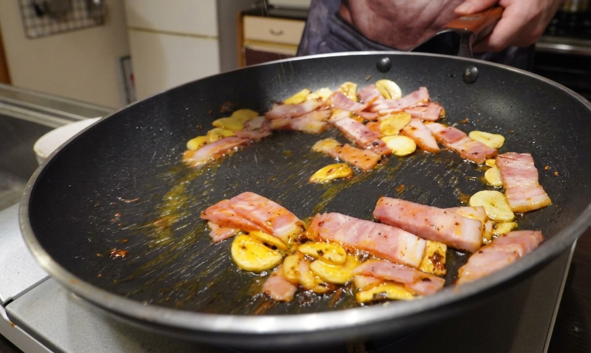 In Scheiben geschnittener Speck, Knoblauch und Chiliflocken braten in einer Pfanne und werden mit frisch gemahlenem schwarzen Pfeffer gewürzt.
