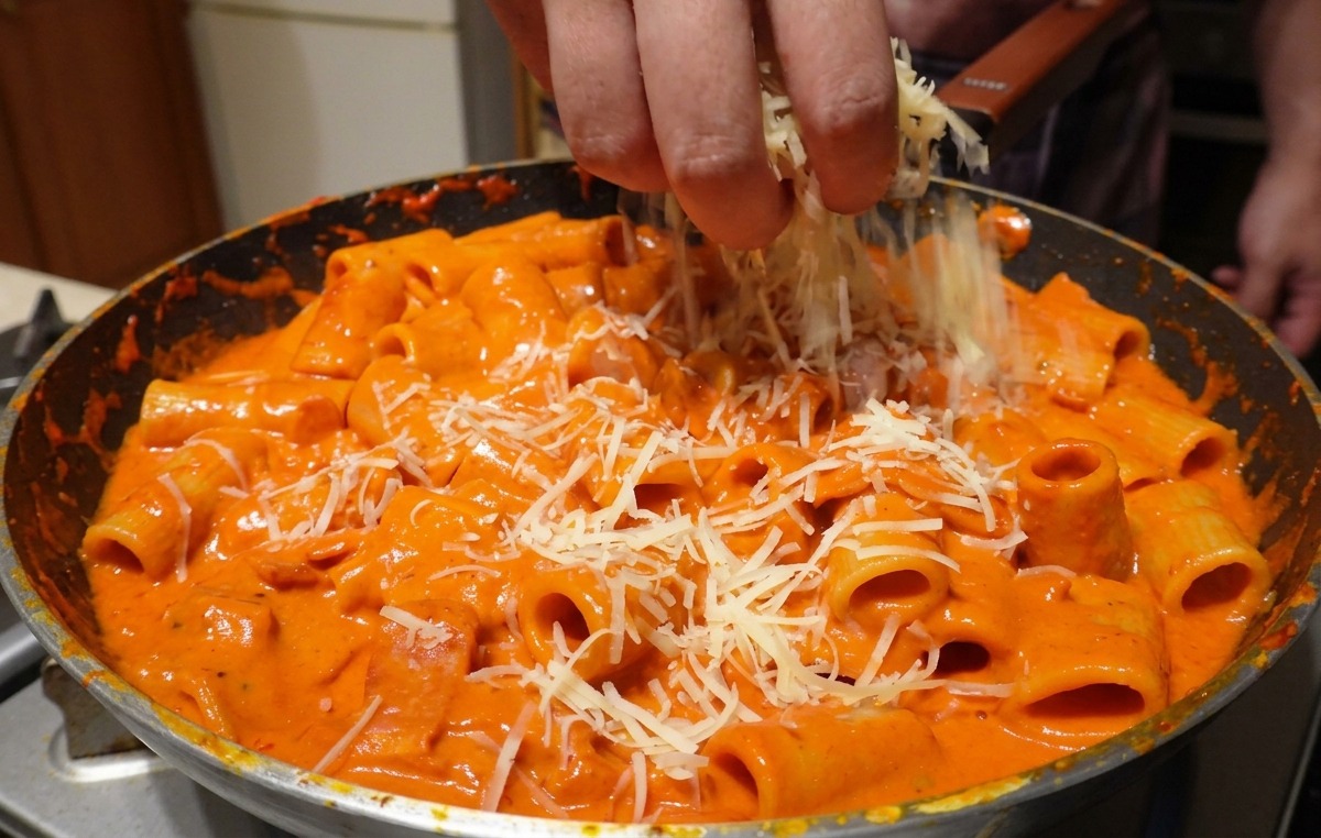 Geriebener Parmesan wird großzügig von Hand über große Rigatoni-Nudeln gestreut, die in einer cremigen rosa Wodka-Sauce gemischt sind.