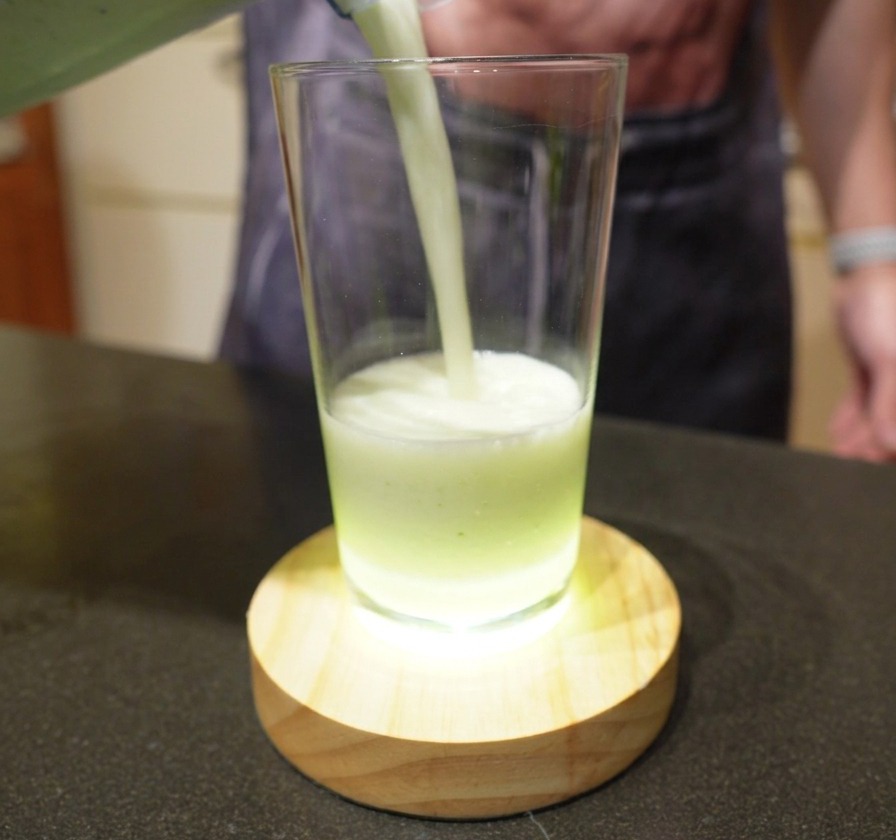 Ein cremiges, blassgrünes Limettengetränk wird aus einem Mixer in ein klares Glas gegossen.