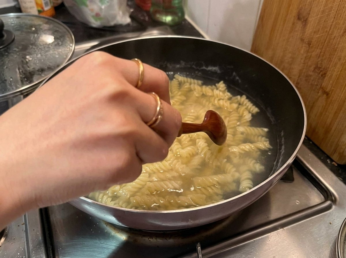 Eine Hand rührt mit einem Holzlöffel gekochte Fusilli in einem Topf mit kochendem Wasser um.