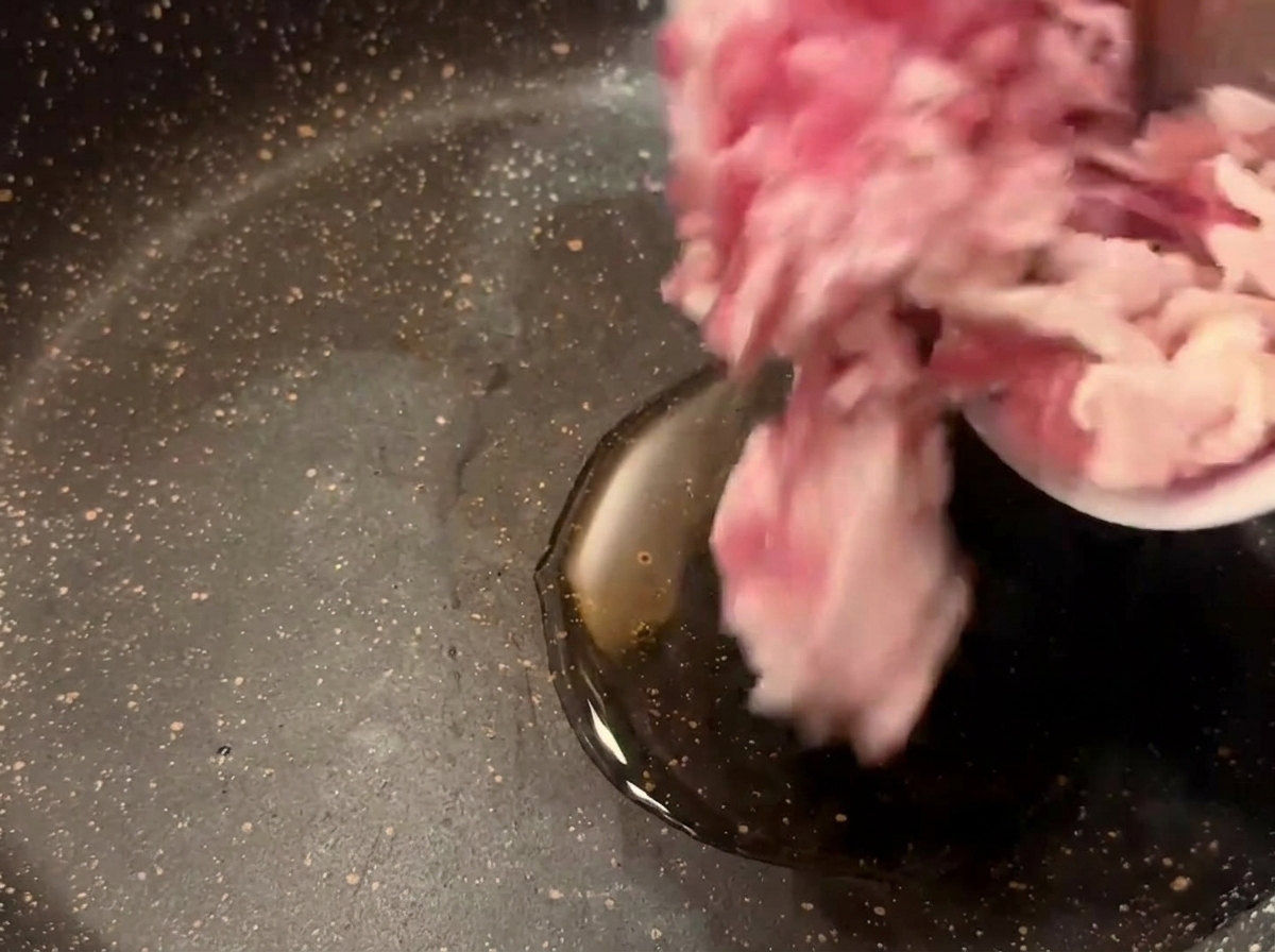 Rohe Speckstücke werden aus einer kleinen Schüssel in eine dunkle Pfanne mit heißem Öl geschüttet.