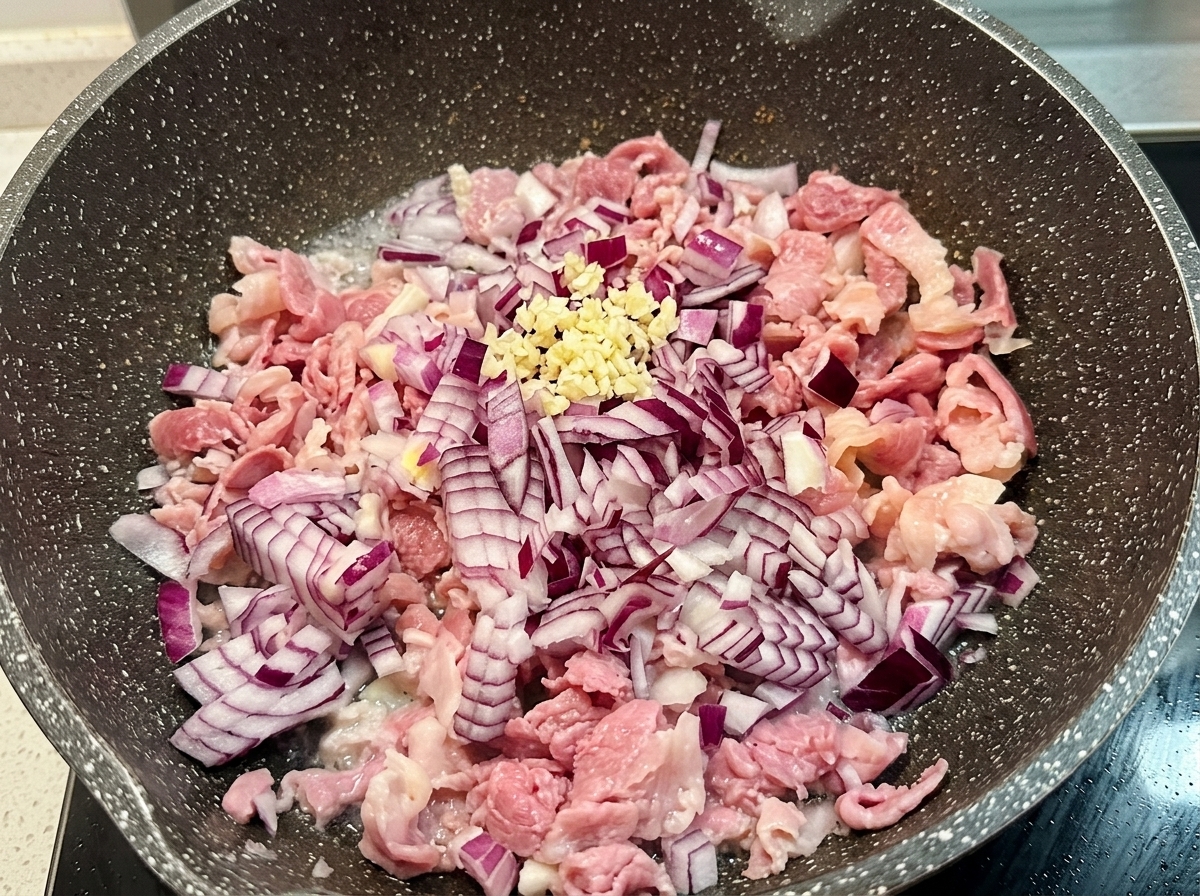 Ein kleiner Haufen frischer gehackter Knoblauch auf den gedünsteten Zwiebeln und dem Speck in der Pfanne.