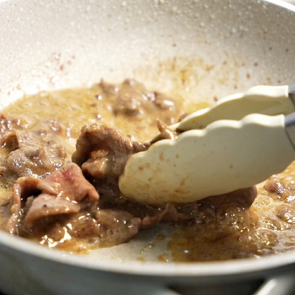Angebratenes Rindfleisch wird mit einer Zange aus der Pfanne gehoben.