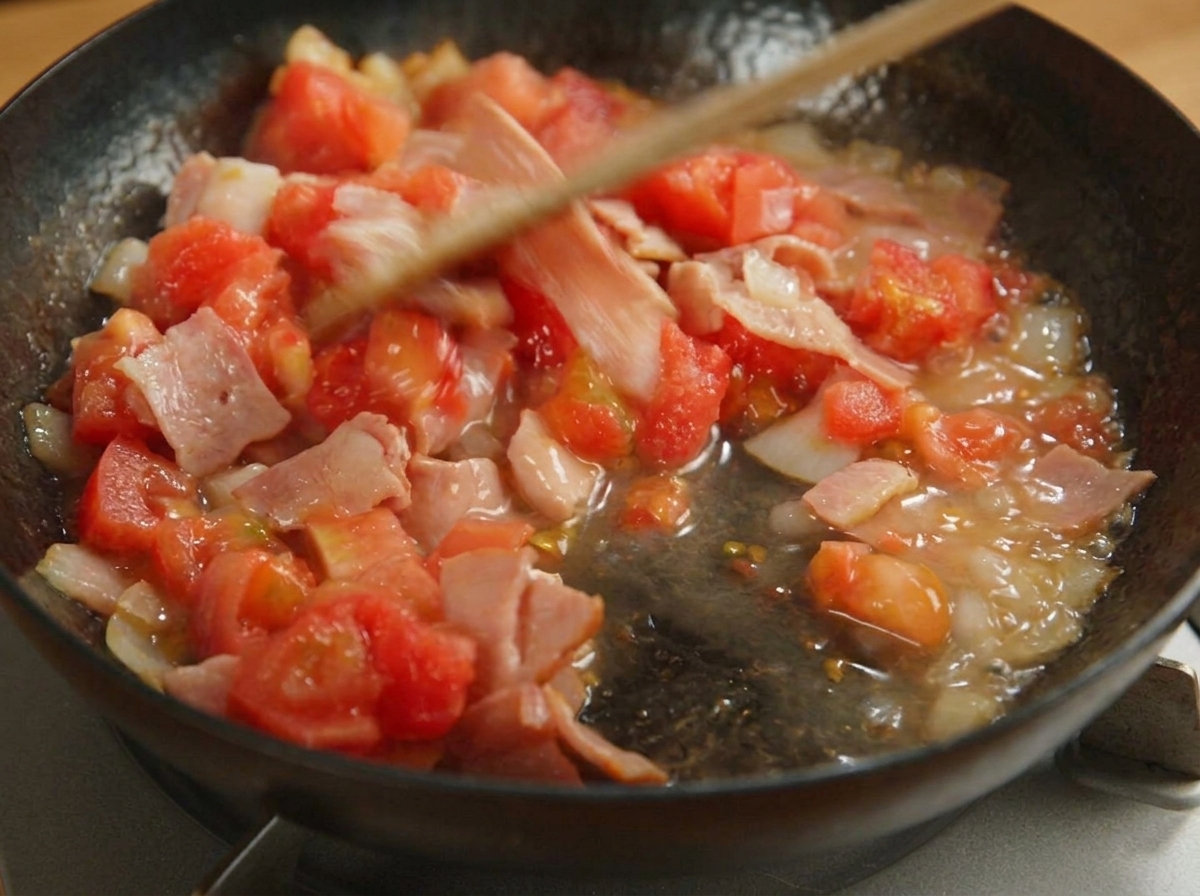 Tomaten, Speck und Zwiebeln werden in der Pfanne zu einer Sauce eingekocht.