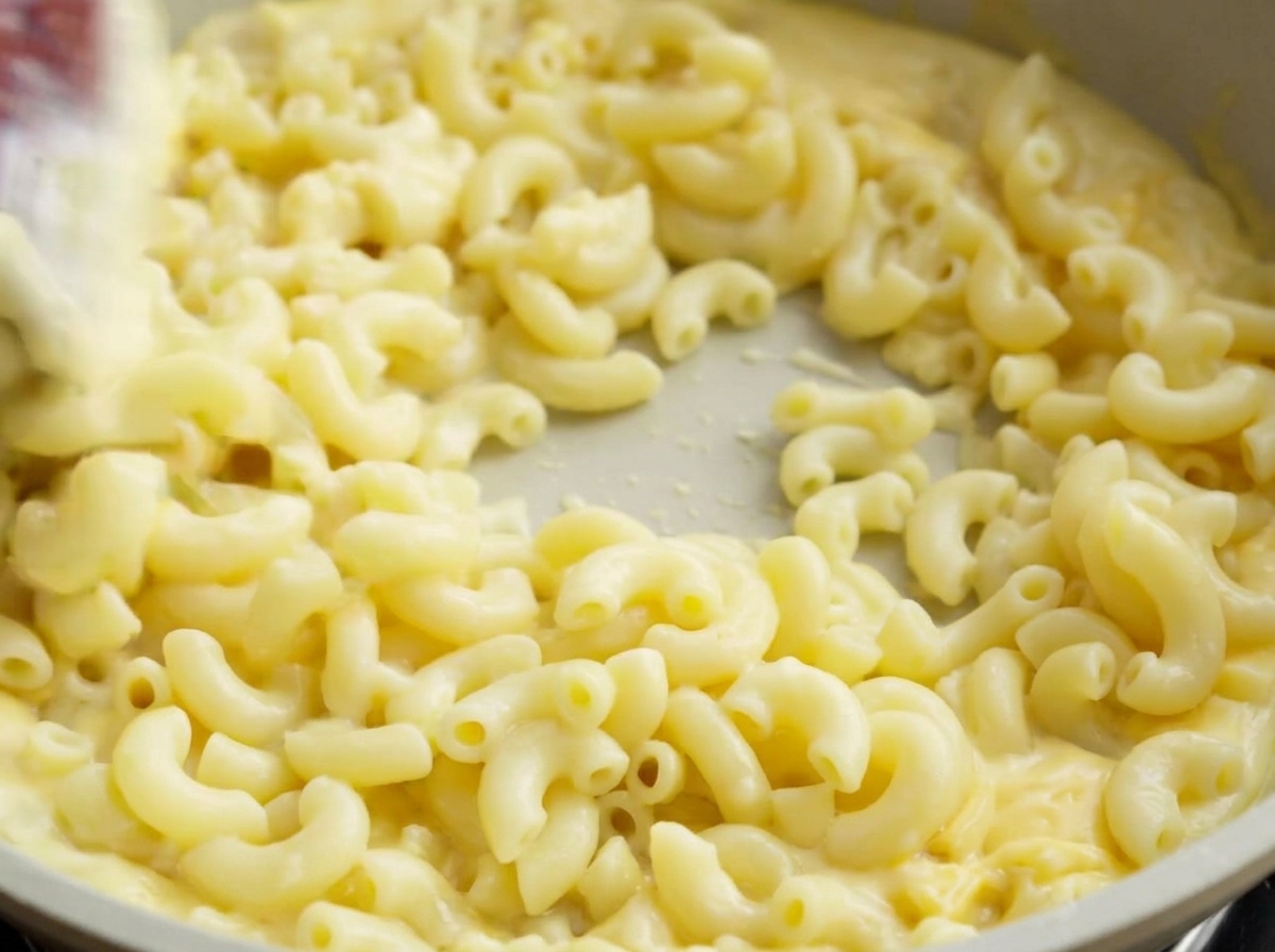 Ein Pfannenwender vermengt die Makkaroni gründlich mit der cremigen Käsesauce.