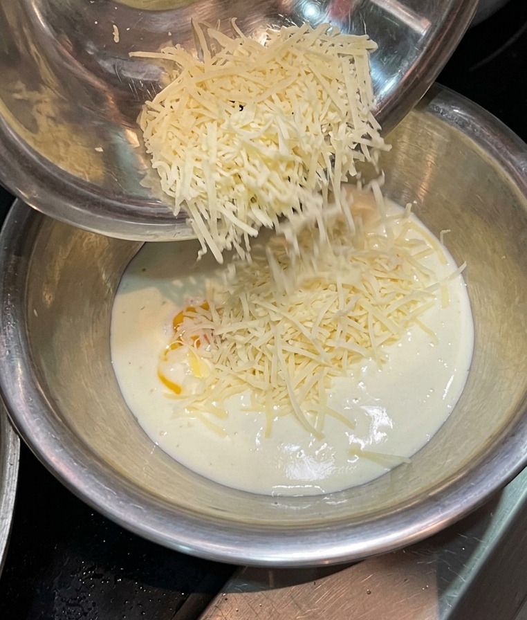 Geriebener Käse fällt in eine Mischung aus Sahne und Eigelb.