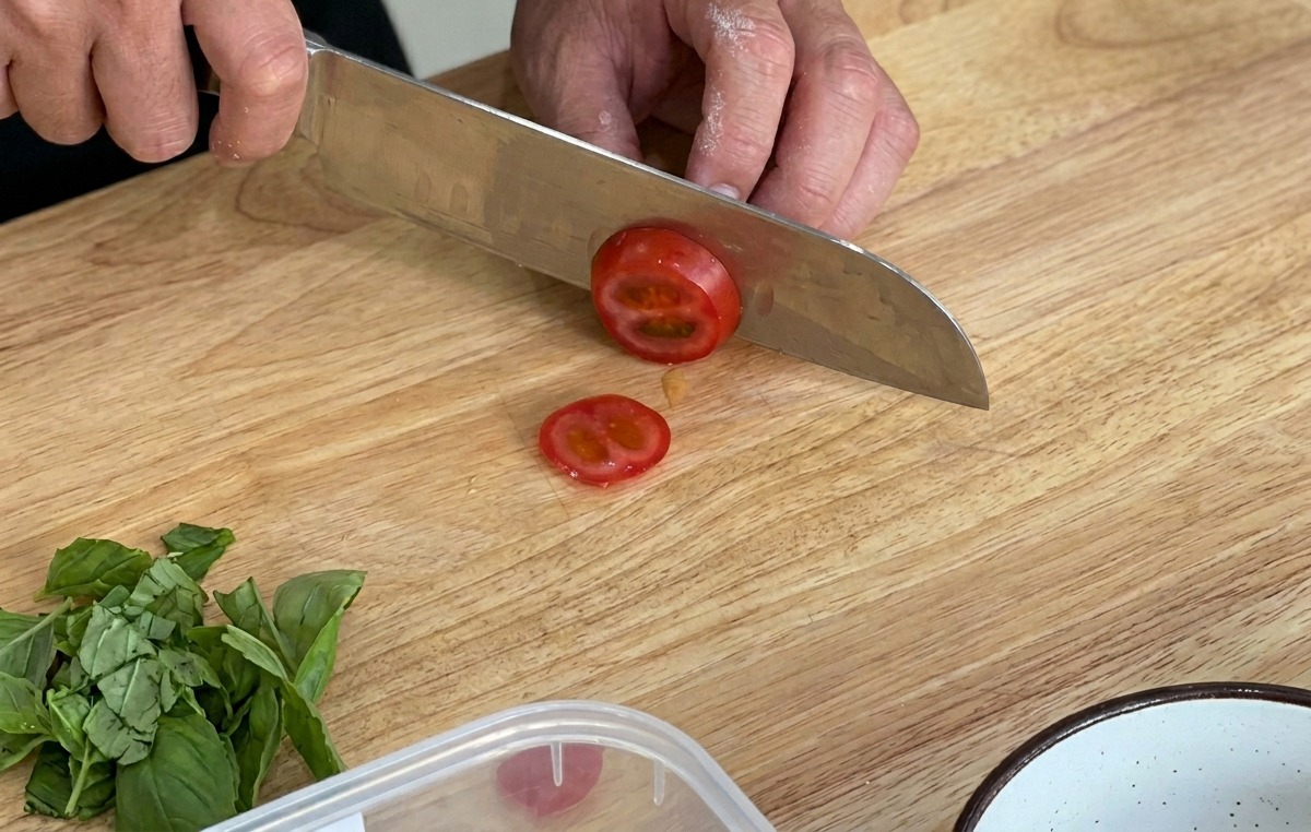 Frische Kirschtomaten werden auf einem Holzbrett in Scheiben geschnitten.