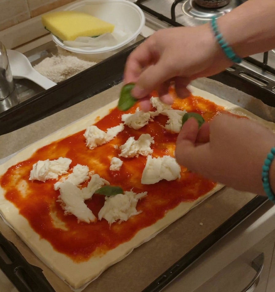 Hände arrangieren frische Basilikumblätter auf einer ungebackenen Pizza mit Tomatensauce und Mozzarella.